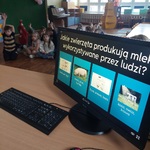 Dzieci siedzą na dywanie, podnoszą ręce by wziąć udział w quizie. 