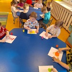 Dzieci siedzą przy stolikach malują palcami.