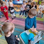 Grupa dzieci siedzi na krzesełkach trzymając pluszowe koty. Chłopiec i dziewczynka badają kota.